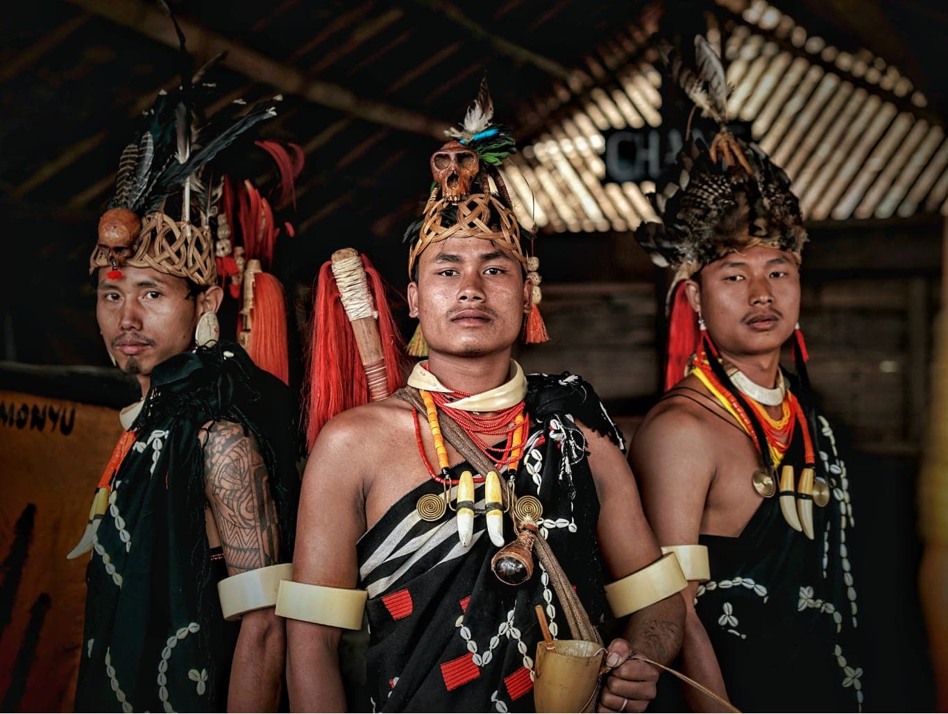 Tiga pemuda berbusana adat dengan hiasan kepala berbulu dan kalung manik-manik