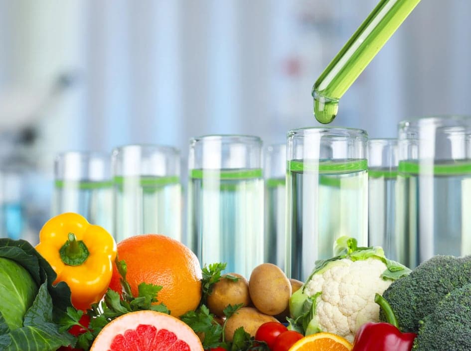 Pipet di atas gelas laboratorium dengan buah dan sayuran segar di depannya